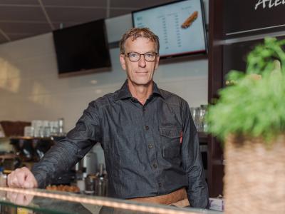 Ondernemer in Kwalitaria-uniform achter de toonbank in een moderne fastfoodomgeving.