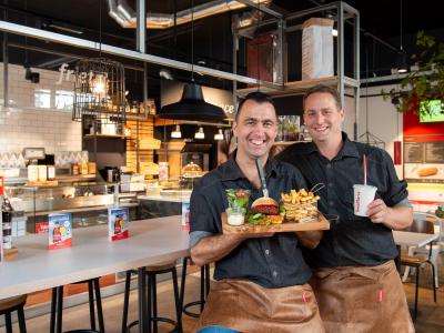 Twee medewerkers van Kwalitaria Délifrance poseren met een burger en frietjes in het restaurant op het Wagnerplein in Tilb...