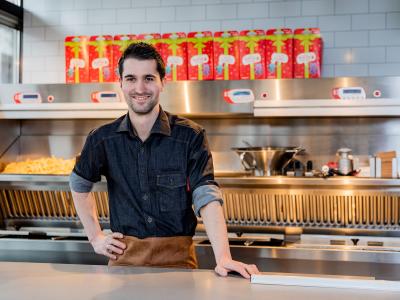 Medewerker in Kwalitaria Prinsenland keuken, omringd door frituurinstallatie en versierde snackdozen.
