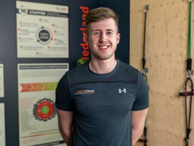 Persoon in sportkleding glimlacht in de nieuwe Personal Fitness Nederland studio in Leiderdorp met posters op de achtergrond.