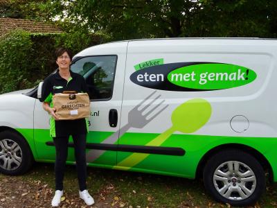 Persoon met een pakket voor een bestelwagen van Eten met Gemak, gefotografeerd buiten met groene achtergrond.