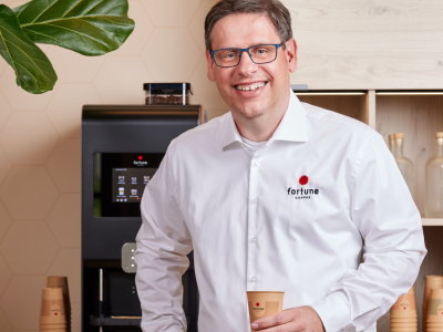 Man in Fortune Coffee-overhemd met koffiebeker voor een koffiemachine in een kantooromgeving.
