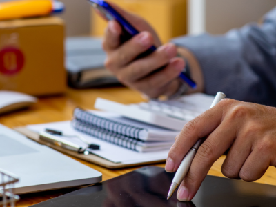 Man werkt aan bureau met tablet, smartphone, notitieboekje en pakketjes rondom zich.