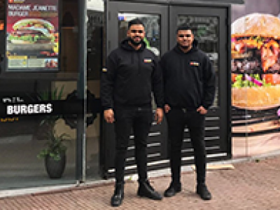 Twee mannen in zwarte kleding staan voor een Spare Rib Express-vestiging met grote burgerposters op de achtergrond.