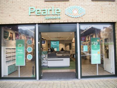 Voorgevel van een Pearle Opticiens winkel met promotieposters in de etalage.