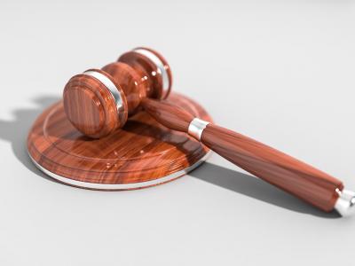 Houten rechterhamer met voetstuk op een grijze ondergrond, symbool voor juridische zaken.