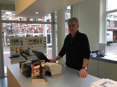 Medewerker staat achter de balie van een nieuw geopende PostMasters-vestiging in Apeldoorn met producten op de achtergrond.