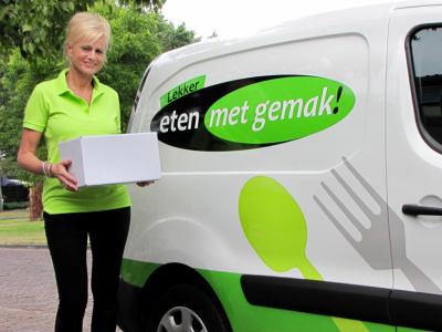 Vrouw in groene kleding met doos naast bestelbus met Eten met gemak-logo.