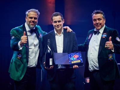 Drie mannen poseren tijdens de Domino’s Awards, twee geven een duim omhoog, de middelste houdt een trofee vast.