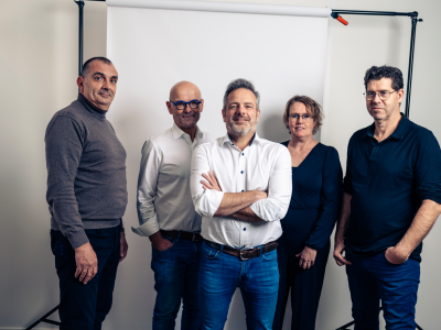 Vijf zakelijke professionals poseren samen voor een neutrale achtergrond in een studio.