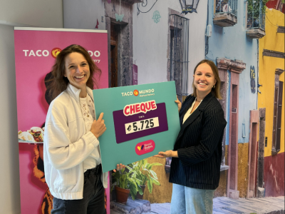 Twee mensen poseren met een cheque van €5.725 in een kleurrijke ruimte bij Taco Mundo.