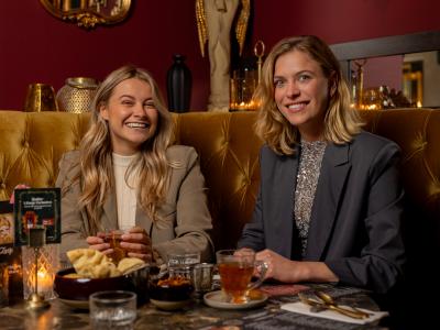 Twee vrouwen lachen terwijl ze genieten van drankjes en hapjes in een stijlvol restaurant.
