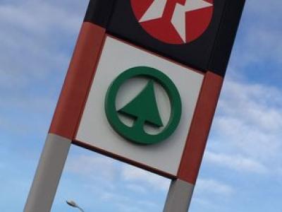 Benzinepomp met Texaco-logo en SPAR-icoon toont brandstofprijzen onder een bewolkte hemel.