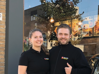 Twee medewerkers bij de ingang van de nieuwe Spare Rib Express-vestiging in Nijkerk, naast een geparkeerde auto.