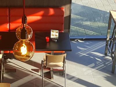 Interieur van een restaurant met houten tafels, rode banken, stoelen en sfeervolle hanglampen.