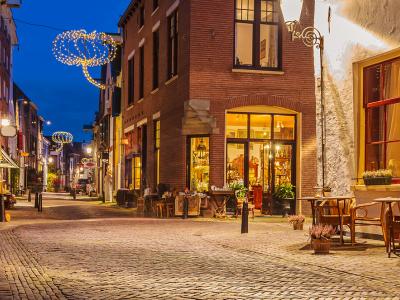 Verlichte winkelstraat in de avond met kerstversieringen en cafés, rustige sfeer.
