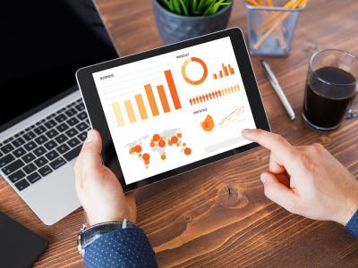 Tablet met grafieken en gegevens over franchisestatistieken 2019 op een bureau met laptop en koffie.