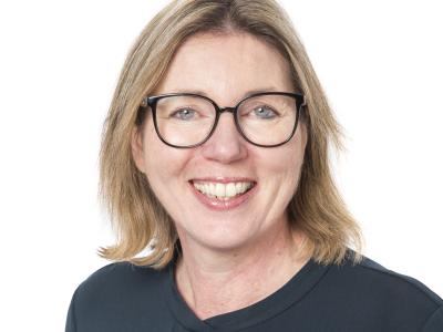 Vrouw met bril glimlacht vriendelijk naar de camera voor een witte achtergrond.