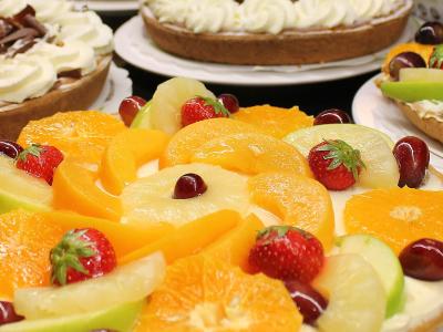 Assortiment van kleurrijke vruchtentaarten van Multi-Vlaai, rijkelijk belegd met vers fruit zoals sinaasappel en aardbei.