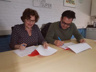 Twee mensen ondertekenen documenten aan een tafel in een kantooromgeving.
