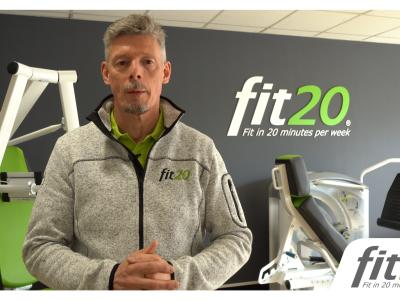 Man in een fit20-sweater voor fitnessapparatuur en fit20-logo op de achtergrond.
