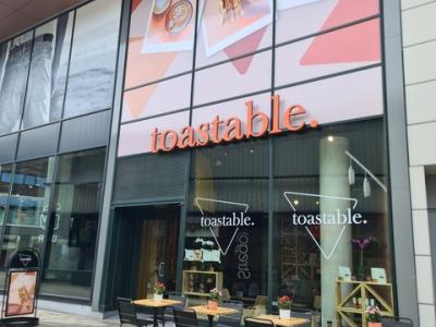 Voorkant van een Toastable-vestiging met zitplaatsen buiten onder een groot uithangbord met op sandwiches.