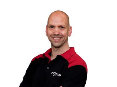 Man in een zwart-rood TOPP-shirt lacht naar de camera voor een witte achtergrond.