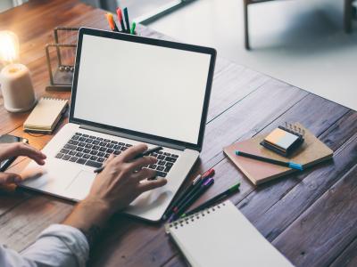 Werkplek met open laptop, notitieblokken, pennen en een Edison-lamp op een houten bureau.