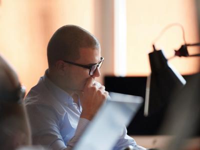 Man met bril denkt na achter een computer in een kantooromgeving.