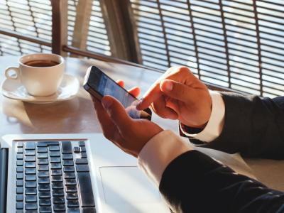 Man in pak werkt met laptop en smartphone in café met kopje koffie op tafel.