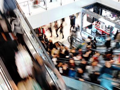 Drukke winkelcentrum met veel mensen op roltrappen en een cosmetica winkel op de achtergrond.