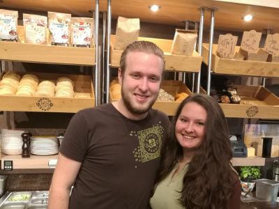 Twee jonge franchisenemers poseren voor een bakkerijdisplay in een Bagels & Beans-filiaal.