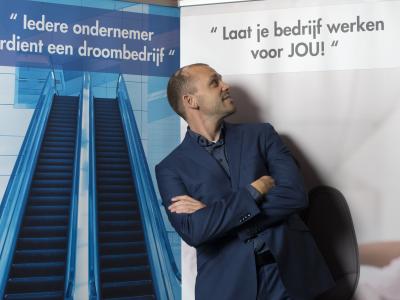 Man in pak kijkt naar inspirerende teksten op een beursstand over ondernemerssucces en bedrijfsoptimalisatie.