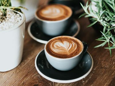 Drie cappuccino's met latte art op een houten tafel omringd door groene planten.