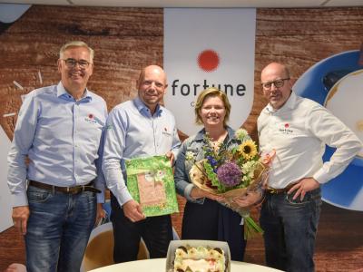 Vier mensen bij Fortune Coffee vieren het 20-jarig jubileum met bloemen en een taart.