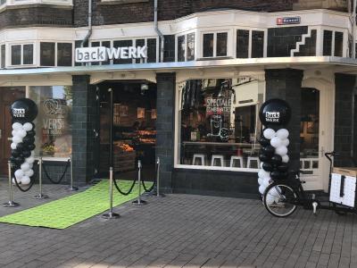 Entree van BackWERK Tilburg met groene loper, ballonnenbogen en bakfiets bij feestelijke opening.