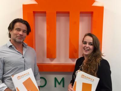 Twee personen houden Domica-mappen vast voor een oranje Domica-logo op de achtergrond.