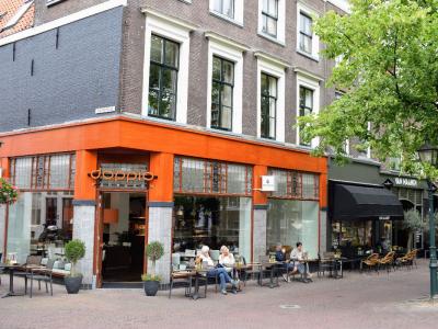 Doppio Espresso-vestiging in Delft met terrastafels en gasten aan de grachtzijde van een historisch pand.