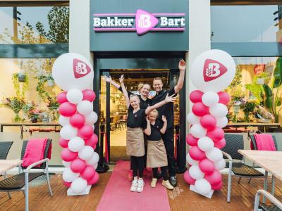 Team Bakker Bart juicht voor de ingang van de nieuwe winkel in Steenwijk, omgeven door bloemen en ballonnen.