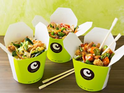 Drie open Eazie takeout-dozen gevuld met kleurrijke noodles en groenten op een tafel met eetstokjes ervoor.
