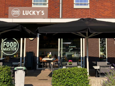Voorkant van Foodmaster Lucky's in Leerdam met terras, zwarte parasols en feestelijke ballonnen.