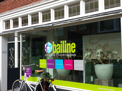 Winkelraam van Bailine met logo en slogans, fiets voor de deur en bloemen in de etalage.