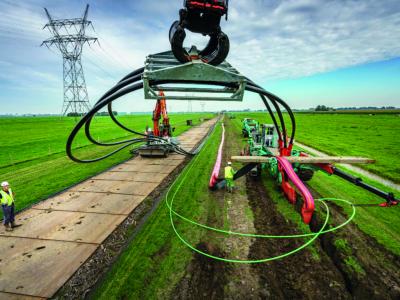 Werkzaamheden in een groen landschap waarbij machines glasvezelkabels in de grond leggen, met hoge elektriciteitsmasten op...