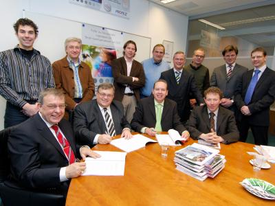 Een groep mannen in zakelijke kleding bij een tafel met papieren en folders in een vergaderruimte van Profile Tyrecenter.