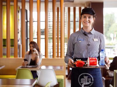 Medewerker in uniform serveert eten op een dienblad in McDonald’s Hardinxveld-Giessendam met klant op de achtergrond.