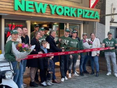 Groepsfoto bij de opening van de nieuwe New York Pizza in Middelharnis met personeelsleden, bloemen en lint.