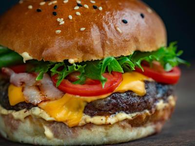 Een close-up van een sappige hamburger met kaas, bacon, sla en tomaat op een broodje met sesamzaadjes.