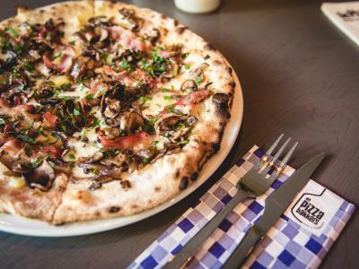 Verse pizza met spek en champignons naast bestek op De Pizzabakkers servet.