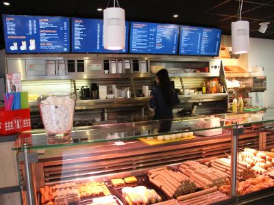 Interieur van Foodmaster met menuborden en vitrine vol snacks, een medewerker staat achter de balie.