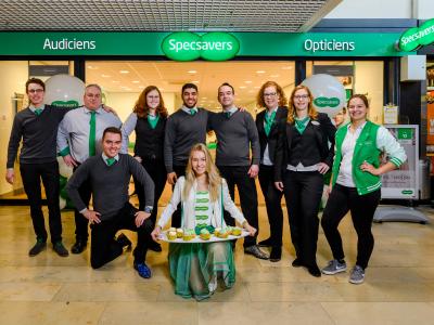 Een team van Specsavers-medewerkers poseert voor de winkel, waarvan de ingang duidelijk zichtbaar is.
